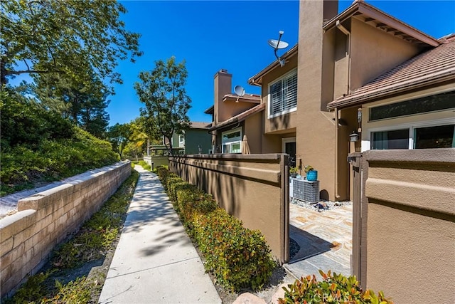 view of side of property with stucco siding, a chimney, and fence