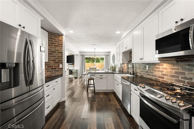kitchen featuring stainless steel appliances, a peninsula, a sink, and dark countertops
