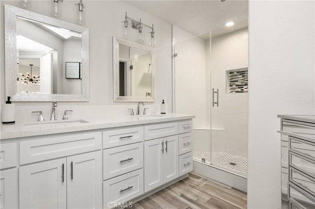 bathroom with double vanity, a stall shower, wood finished floors, and a sink