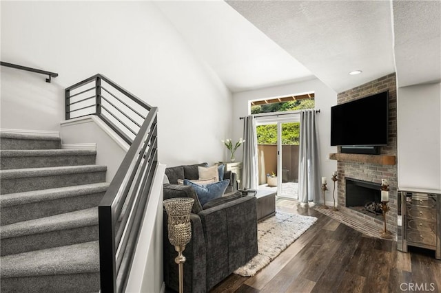living area featuring dark wood finished floors, a brick fireplace, stairs, a textured ceiling, and high vaulted ceiling
