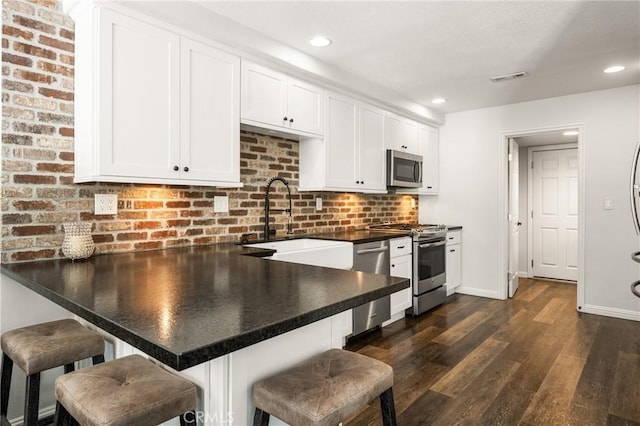 kitchen featuring a peninsula, a sink, visible vents, white cabinetry, and appliances with stainless steel finishes
