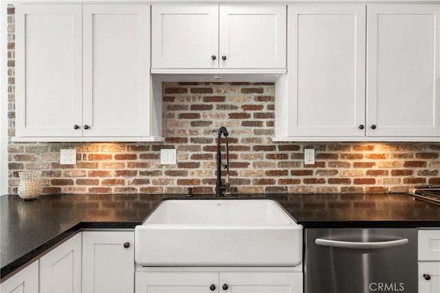 kitchen featuring white cabinets, stainless steel dishwasher, a sink, dark countertops, and decorative backsplash