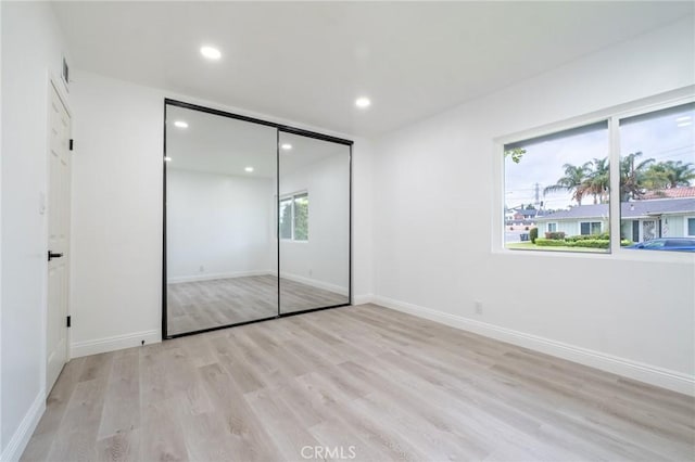 unfurnished bedroom with baseboards, recessed lighting, a closet, and light wood-style flooring