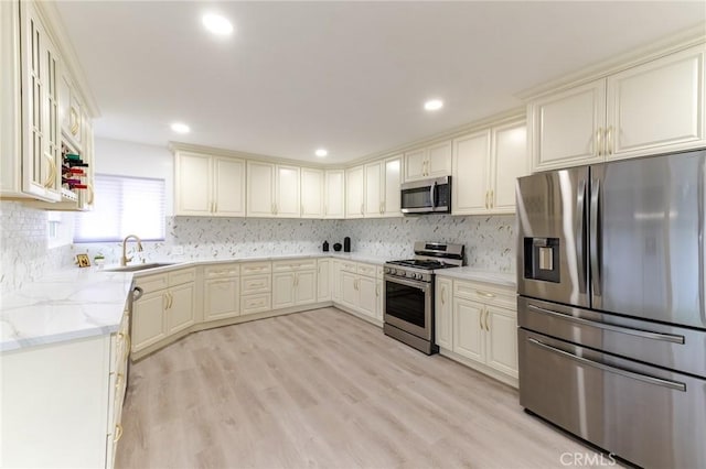 kitchen featuring light stone counters, tasteful backsplash, a sink, light wood-type flooring, and stainless steel appliances