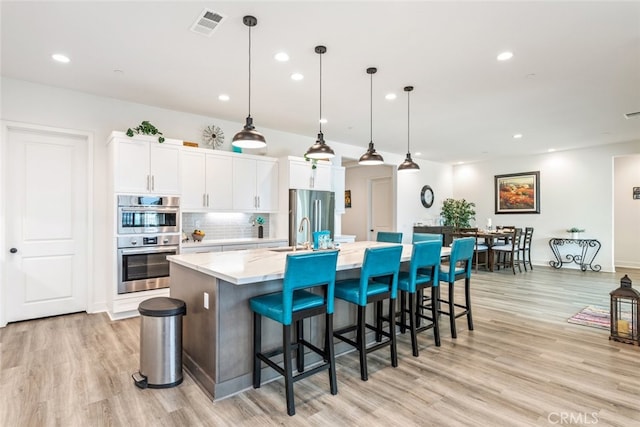 kitchen with a large island, visible vents, white cabinets, light wood finished floors, and stainless steel appliances