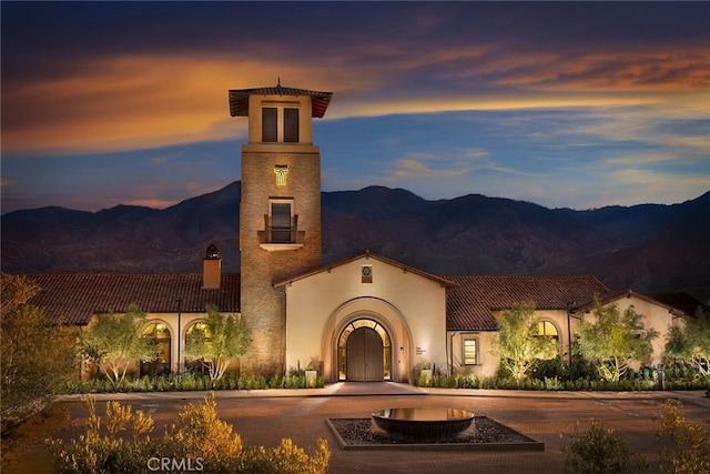view of front facade with curved driveway, a mountain view, a chimney, and stucco siding