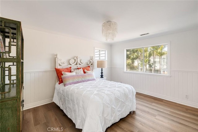bedroom featuring a wainscoted wall, visible vents, and wood finished floors