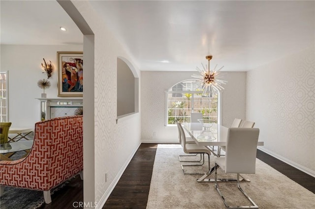 dining room with dark wood-style flooring, a notable chandelier, baseboards, arched walkways, and wallpapered walls