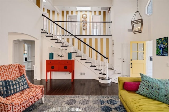 living area with wood finished floors, arched walkways, stairs, and a high ceiling