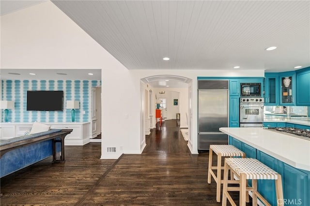 kitchen featuring blue cabinets, glass insert cabinets, a breakfast bar, light countertops, and built in appliances