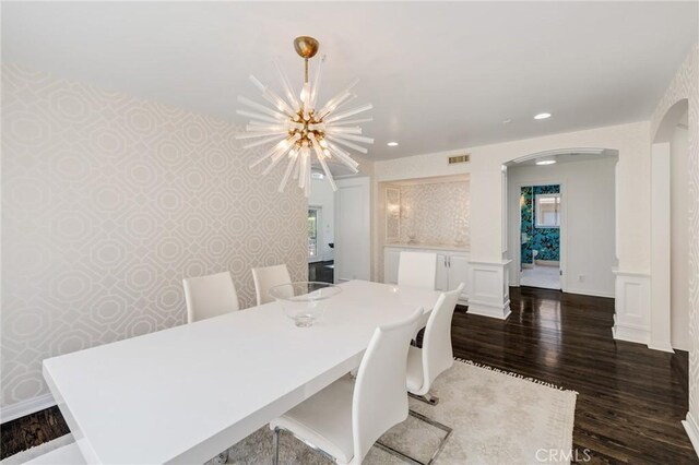 dining room with an inviting chandelier, dark wood-type flooring, visible vents, arched walkways, and wallpapered walls
