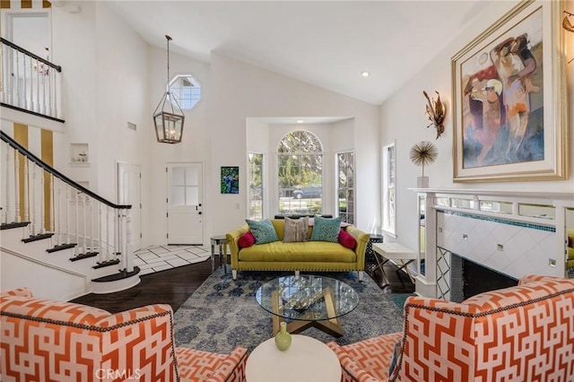 living room featuring stairs, high vaulted ceiling, wood finished floors, and a fireplace