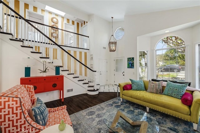 living room with stairs, visible vents, baseboards, a towering ceiling, and wood finished floors