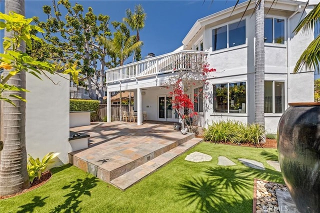 rear view of house with stucco siding, a lawn, a patio area, and heating fuel