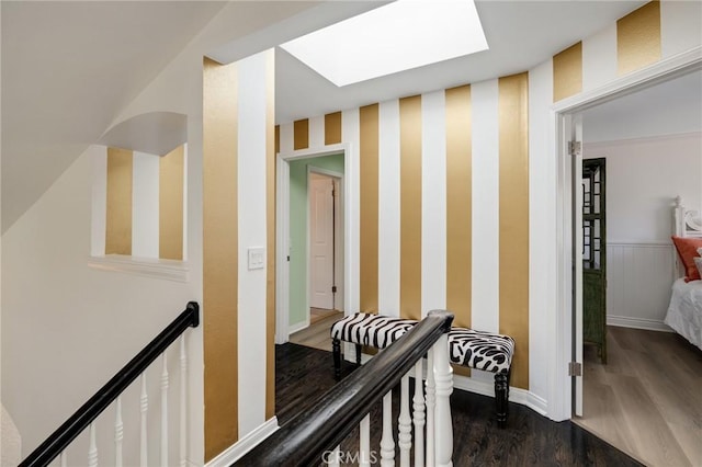 hallway featuring baseboards, wallpapered walls, a skylight, and dark wood-style flooring