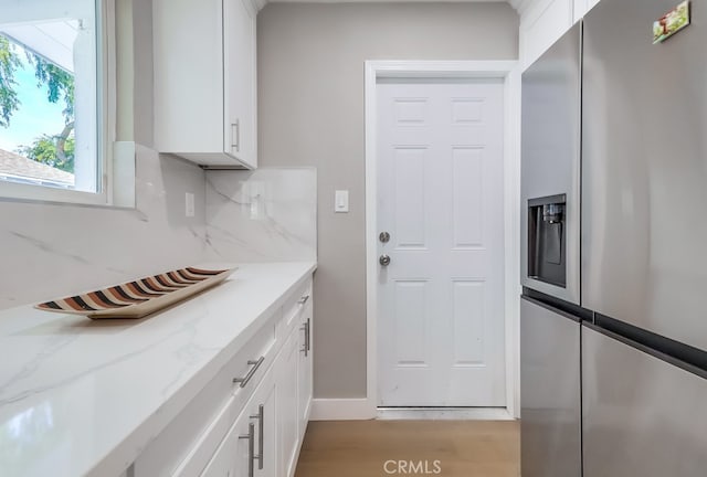 kitchen featuring light wood finished floors, light stone countertops, stainless steel fridge, backsplash, and white cabinetry