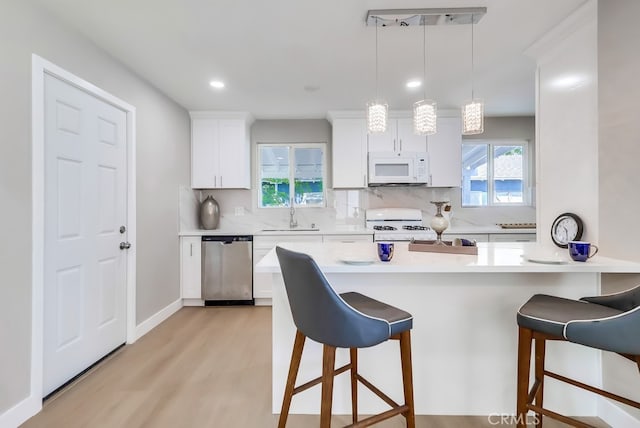 kitchen with a breakfast bar area, white appliances, light wood-style flooring, and a sink