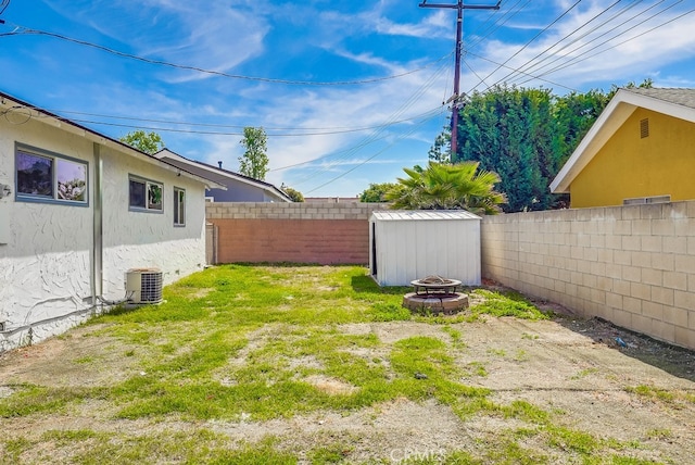 view of yard with an outdoor fire pit, a fenced backyard, central AC unit, and a storage shed