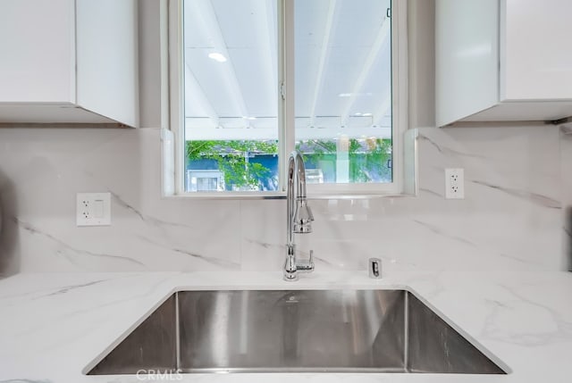 details with light stone countertops, a sink, white cabinetry, and tasteful backsplash