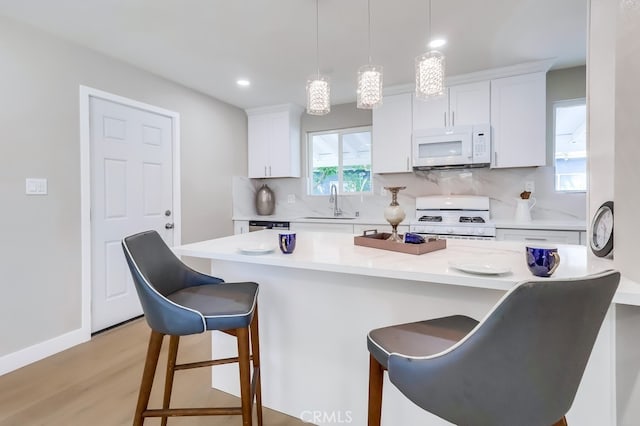 kitchen with a kitchen breakfast bar, white cabinetry, light wood-style flooring, white appliances, and backsplash
