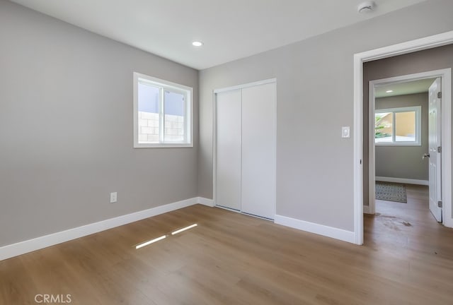 unfurnished bedroom featuring recessed lighting, a closet, wood finished floors, and baseboards