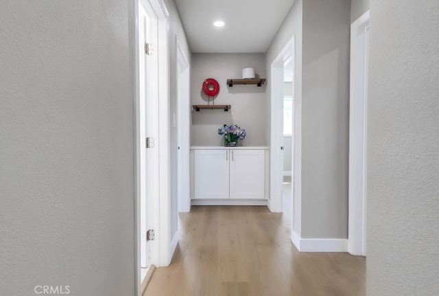 hallway with baseboards, light wood-type flooring, and a textured wall
