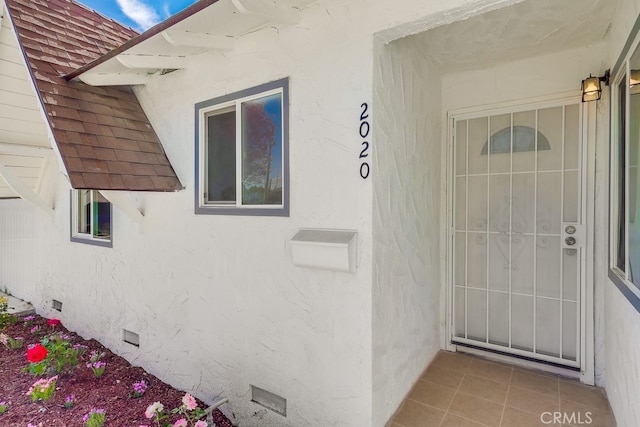 doorway to property with stucco siding, roof with shingles, and crawl space