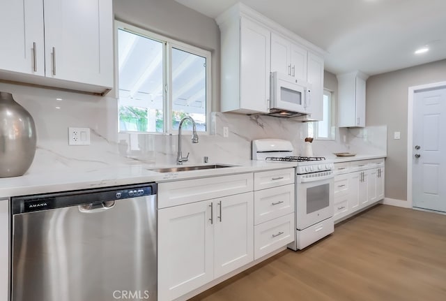 kitchen featuring white appliances, decorative backsplash, white cabinets, a sink, and light wood-type flooring