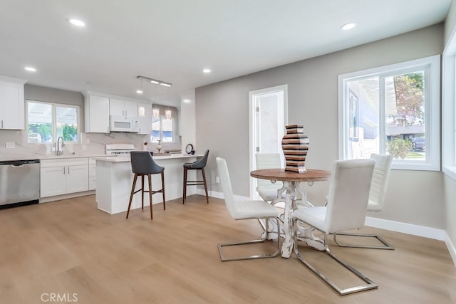 kitchen featuring recessed lighting, white microwave, light wood-style flooring, dishwasher, and a kitchen bar