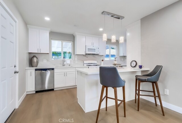 kitchen with a sink, light wood-style floors, stove, white microwave, and stainless steel dishwasher
