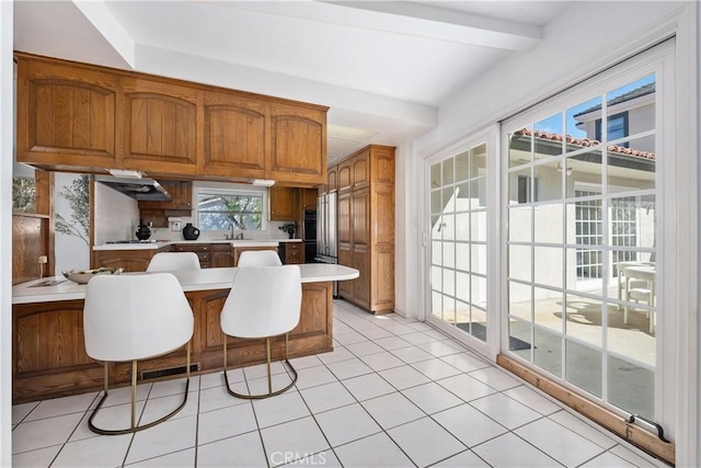 kitchen featuring a peninsula, high end refrigerator, light countertops, brown cabinets, and a sink