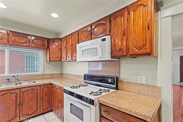 kitchen featuring light countertops, a sink, brown cabinets, and white appliances