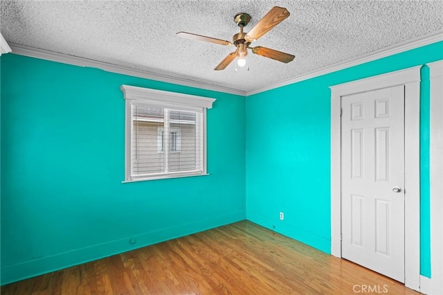 unfurnished room featuring a textured ceiling, crown molding, ceiling fan, baseboards, and wood finished floors