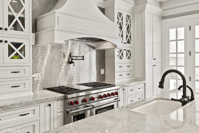 kitchen with white cabinets, range with two ovens, custom exhaust hood, and a sink