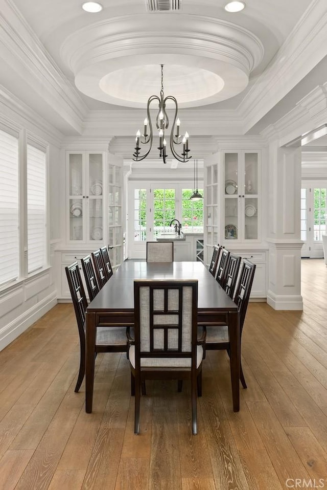 dining space with french doors, ornamental molding, light wood-type flooring, an inviting chandelier, and a raised ceiling