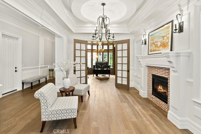 sitting room with a tray ceiling, a chandelier, a decorative wall, and hardwood / wood-style flooring