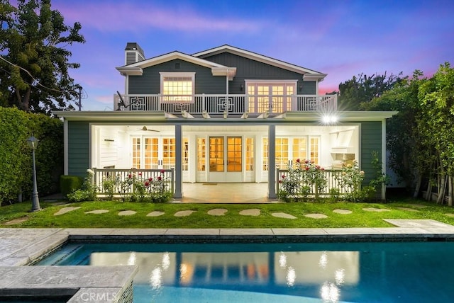 back of house featuring a patio, an outdoor pool, a chimney, and a balcony