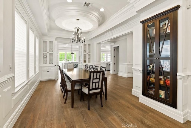 dining space featuring a notable chandelier, visible vents, a decorative wall, crown molding, and a raised ceiling