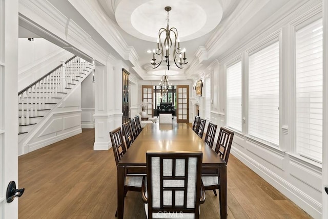 dining area with a notable chandelier, stairs, a decorative wall, wood finished floors, and ornate columns