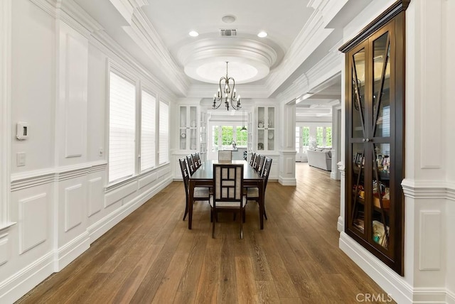 dining space with ornamental molding, dark wood finished floors, an inviting chandelier, a decorative wall, and a raised ceiling