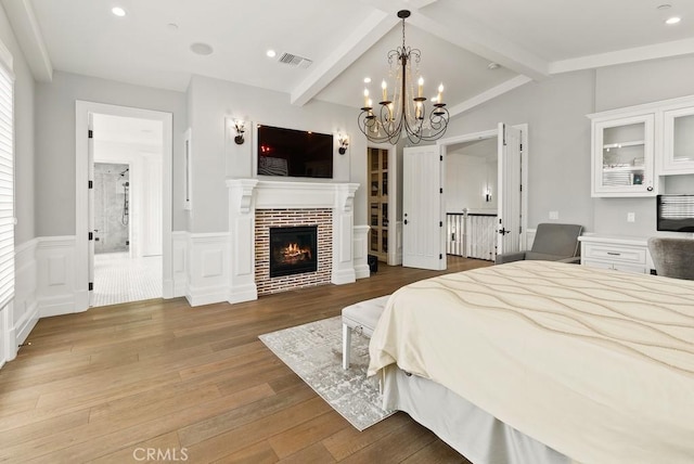 bedroom featuring a warm lit fireplace, visible vents, a chandelier, a wainscoted wall, and wood finished floors