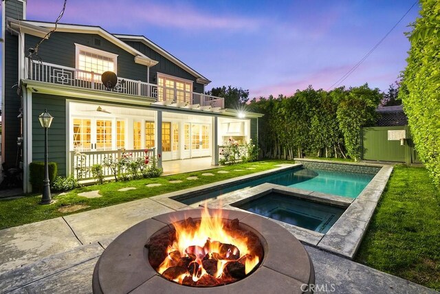 back of property at dusk with an outdoor pool, a balcony, a patio, an in ground hot tub, and an outdoor fire pit