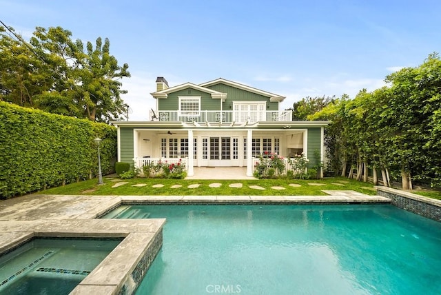 back of house with a patio area, an outdoor pool, a balcony, a chimney, and a lawn
