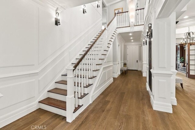 stairway featuring ornamental molding, a decorative wall, wood-type flooring, and ornate columns