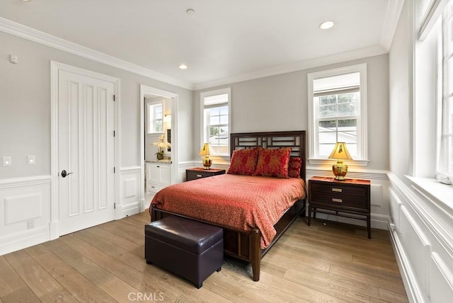 bedroom with a decorative wall, crown molding, and light wood-style flooring