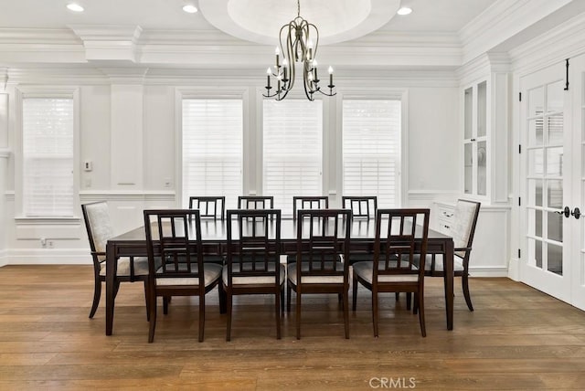 dining room with a decorative wall, french doors, wood finished floors, ornamental molding, and a chandelier