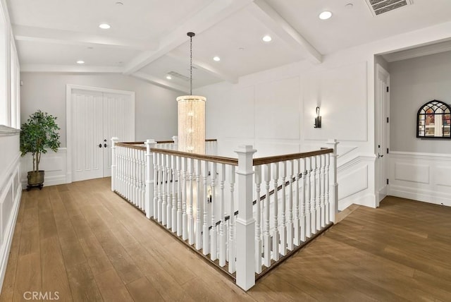 hallway featuring an upstairs landing, visible vents, a decorative wall, and hardwood / wood-style floors