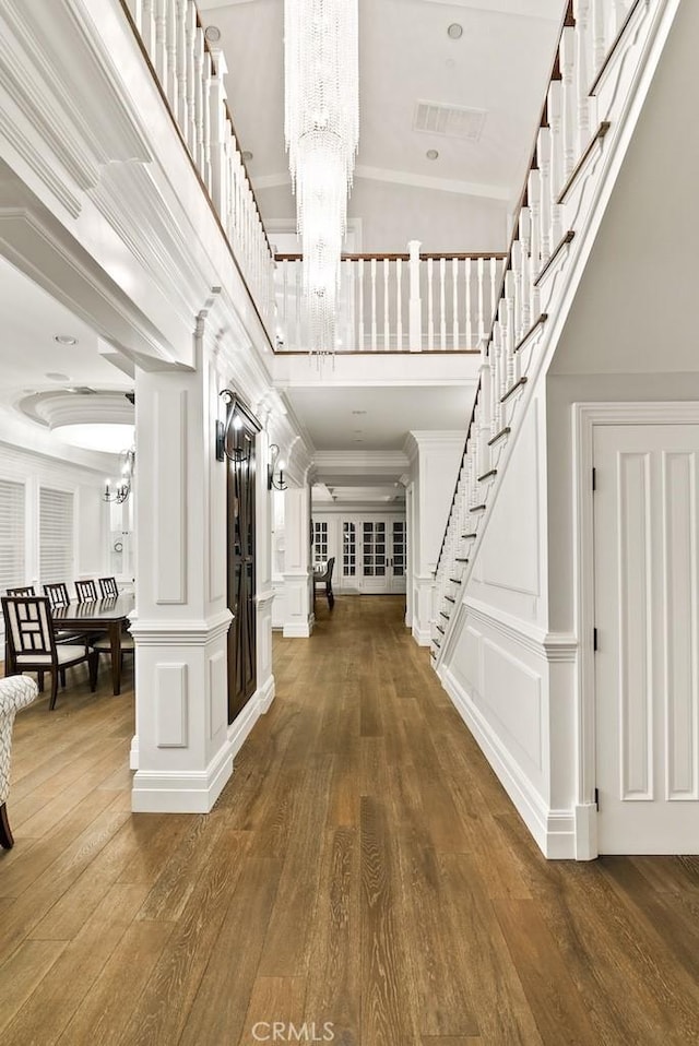 entryway featuring stairs, a decorative wall, wood finished floors, visible vents, and an inviting chandelier