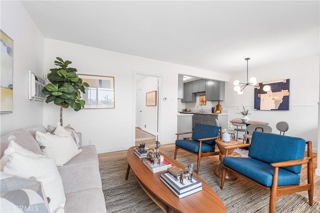 living room with an inviting chandelier, light wood-style floors, a wall mounted air conditioner, and baseboards