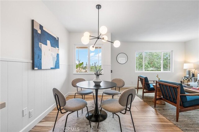dining room with a wainscoted wall, a notable chandelier, and light wood-style floors